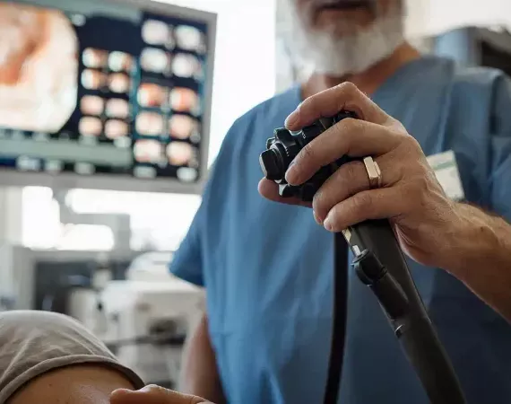 Magenspiegelung - Arzt hält Instrument, Patient liegt seitlich, im Hintergrund sieht man den Monitor.