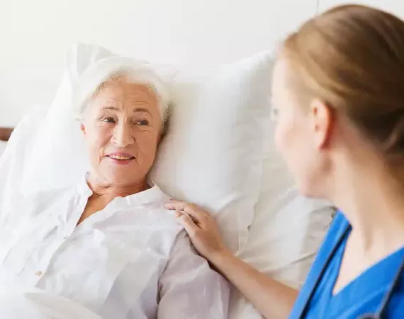 Seniorin im Krankenhausbett, Ärztin oder Schwester legt ihr die Hand auf die Schulter.