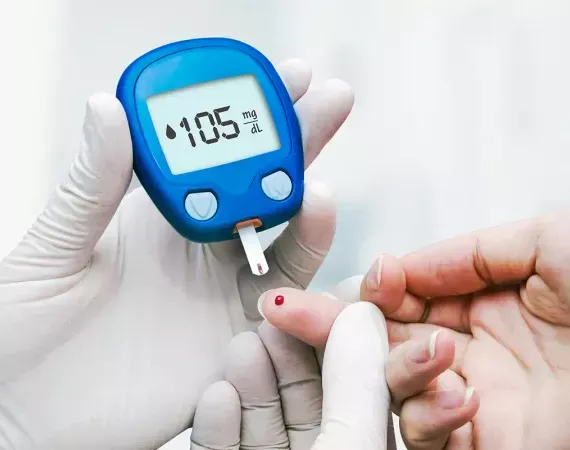 Person mit Handschuhen testet Blutzuckerspiegel mit Teststreifen, Wert 105; auf der Fingerspitze des Patienten ein kleiner Blutstropfen.