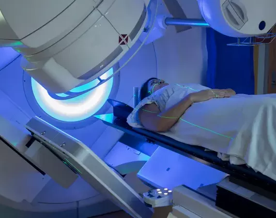 Frau während der Brustkrebs-Bestrahlung im Gerät liegend, blauer Lichtschein.