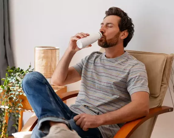 Mann sitzt auf einem Sessel und trinkt probiotischen Trinkjoghurt.